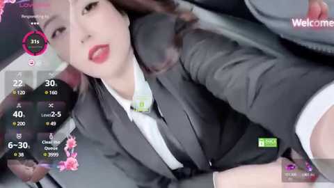 Media: A video of an East Asian woman with fair skin, wearing a gray business suit, smiling seductively while driving, with a digital speedometer overlay.