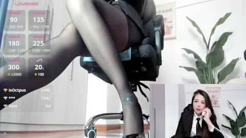 Media: A video of a seductive woman in a black skirt and stockings, reclining on a chair in a modern office, with a video feed of an Asian woman in a black suit and white shirt, sitting at a desk.