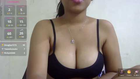 Media: Video of a young Asian woman with medium skin tone, wearing a black bra that accentuates her large breasts. She has long, black hair tied back. Background shows a digital screen displaying a game with various stats.