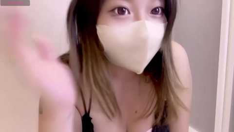 Media: A video of an Asian woman with long, straight, dark brown hair, wearing a white face mask and a black lace bra, looking up with wide eyes, blurred background.