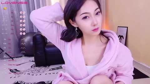 Media: Video of an East Asian woman with fair skin and dark hair, wearing a light pink robe, sitting on a black leather chair.