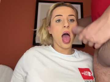 Media: A video of a blonde woman in a white t-shirt with a red logo, mouth open, tongue out, in a room with red walls and framed art.