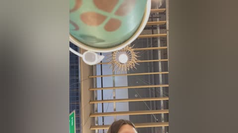 Media: Video of a person with brown hair, viewed from above, standing in a modern, industrial space with a metal staircase, green lamp, and white light fixture.