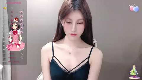 Media: A video of a young Asian woman with pale skin, long brown hair, and a slender physique, wearing a black spaghetti-strap dress, sitting indoors against a plain gray wall.