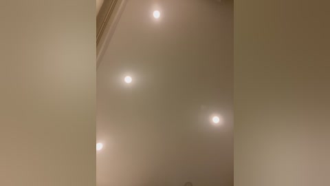 Media: Video of a ceiling with four bright, circular lights emitting a soft, diffused glow, creating a warm, inviting atmosphere. The ceiling is painted a light beige color, contributing to the cozy ambiance. The image captures a minimalist, well-lit room.