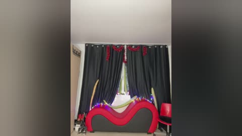 Media: Video of a modern, minimalistic bedroom with a black and red bed, dark curtains, and a vibrant red chair.