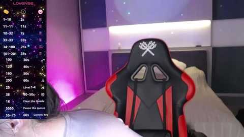 Media: Video of a gaming streamer, seated in a red and black gaming chair, with a white and purple backdrop, displaying a Twitch chat feed on the left.