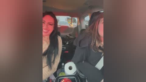 Media: A video shows two women in a car, smiling and laughing, with the front view partially blurred. They are dressed in warm clothing, and the car interior is cluttered with personal items.