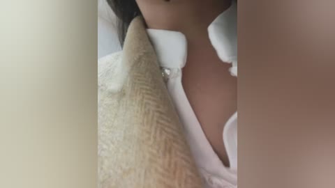 Media: Video showing a close-up of a woman's neck and chest, wearing a white blouse with a high collar. A beige, textured scarf is partially draped over her shoulder. The image is cropped and slightly blurry.