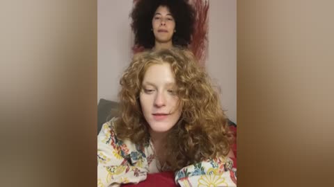 Media: Video of a white woman with curly hair and a red shirt, sitting on a red couch, with a Black woman with natural hair standing behind her.