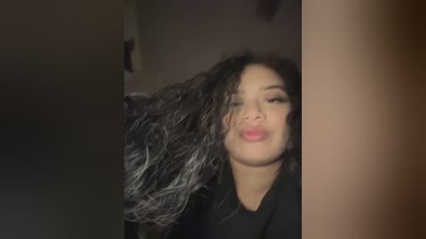 Media: A video of a young woman with long, wavy black hair blowing in the wind, partially obscured by a vertical column. She has light skin and a neutral expression.