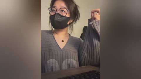 Media: Video of an Asian woman in glasses and a black mask, holding a gray sweater, indoors with blurred background.