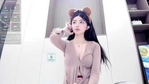 Media: Video of an Asian woman with long black hair, wearing a beige cardigan, holding a phone to her ear, in a modern, minimalist room with a white wall and a calendar.