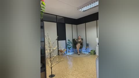 Media: Video of a woman in a dark, knee-length dress, standing in a modern office with beige carpet, white walls, and a glass partition.