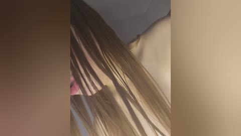 Media: A video showing a close-up of a woman's long, straight, light brown hair with pink highlights, partially obscuring her face, set against a beige wall.