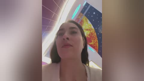 Video of a young woman with dark hair, wearing a white top, standing in a brightly lit, futuristic room with tiled walls and vibrant, abstract art.