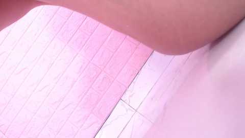 Media: A close-up video of a person's hand and arm, with a pink tiled bathroom wall in the background. The skin tone is light, and the tiles have a subtle white pattern.