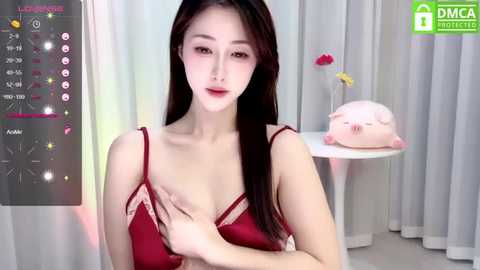 Media: Video of an East Asian woman with long black hair, wearing a red lace lingerie set, sitting in a white room with pink and yellow decorations.