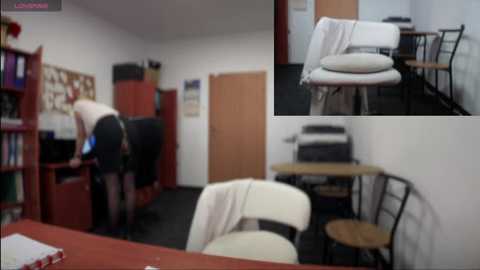 Media: Video of a messy office with a white chair, beige cushion, and a white table, and a person in a black skirt bending over a red bookshelf.