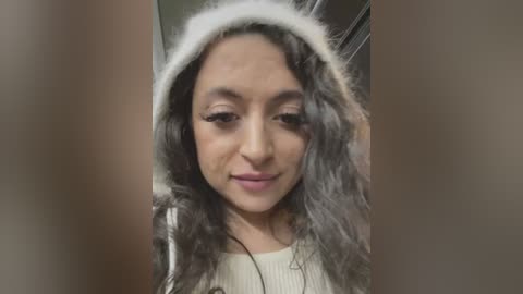 Media: Video of a young woman with medium brown skin, long curly gray hair, wearing a white fur hooded jacket, smiling.