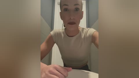 Media: A video of a light-skinned woman with short, platinum blonde hair, wearing a beige crop top, taken from a low angle, showing her from the waist up.