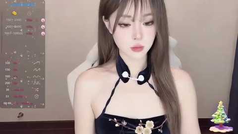 Media: Video of a young Asian woman with long brown hair, wearing a black halter top with a large bow, against a beige wall with a digital clock.