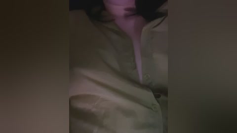 Media: Video of a man's torso wearing a beige button-down shirt, slightly unbuttoned, revealing a hint of a white undershirt. The lighting casts shadows, creating a moody, intimate atmosphere.