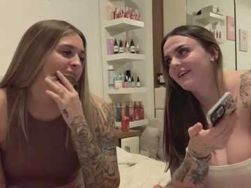 Media: Video of two tattooed women with long brown hair, in a beauty salon. One holds a phone, the other touches her face. Background shows shelves filled with beauty products.