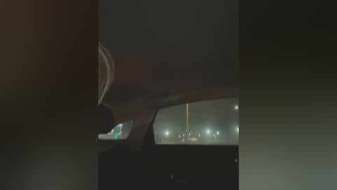 Media: Video of a dimly lit car interior at night, with a blurred highway scene outside, featuring faint headlights and distant streetlights. The car's window is partially open, revealing a dark, shadowy view.