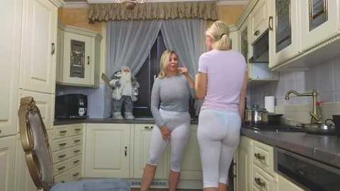 Media: A video shows two blonde women in tight, light gray workout gear laughing in a modern, cream-colored kitchen.