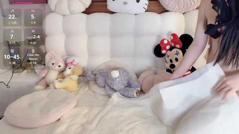 Media: Video of a plush-filled bed with a Minnie Mouse doll, a teddy bear, and a bunny, featuring a person in a white robe, blurred.