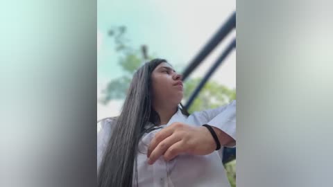 Media: Video of a young woman with long, straight black hair, wearing a white shirt, captured from a low angle, showing her profile.