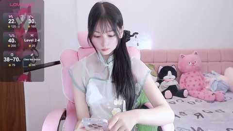 Media: A video of an Asian woman with long black hair in a pink gaming chair, holding a controller in a cozy bedroom with plush toys.