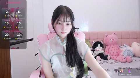 Media: Video of an East Asian woman with long black hair, wearing a see-through white dress, sitting in a pink gaming chair in a pastel-colored room.