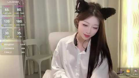 Media: Video of an East Asian woman with long black hair, wearing black cat ear headband, white blouse, and sitting indoors.