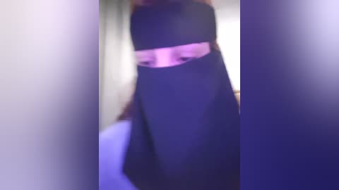 Media: Blurry video of a person in a black dress with a pink sash, partially obscured by a window frame. Background is indistinct, with a hint of a white wall.