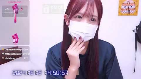 Media: A video shows a young Asian woman with long, straight, dark hair wearing a surgical mask and a blue cape, in a sterile, white-walled room. The background includes a \"Lounge\" screen displaying a pink hairbrush.