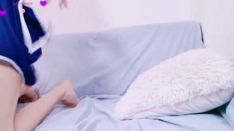 Video of a pale-skinned woman in a blue and white sailor outfit kneeling on a light blue bed with a fluffy pillow.