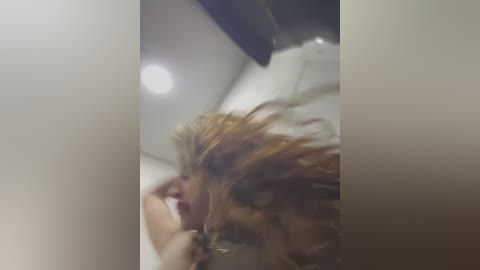 Media: A blurry video shows a close-up of a person with messy, blonde hair, lying on a bed, with a ceiling light in the background.