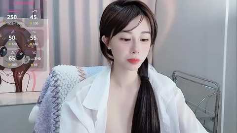 Media: A video of an East Asian woman with long, dark hair, fair skin, and red lipstick, wearing a white lab coat, sitting in a medical setting with a blurred background and a thermometer display.