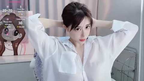 Media: A video of an East Asian woman with medium-length brown hair, wearing a white shirt and adjusting her collar. Background features a poster and a grey wall.