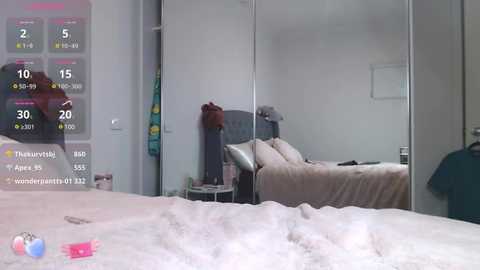 Media: Video of a modern bedroom with a large mirror reflecting a neatly made bed, featuring white sheets and a dark headboard. A weather overlay displays temperature and humidity data.