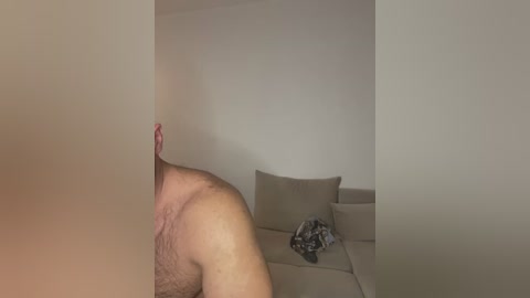 Media: Video of a man's uncircumcised penis, partially obscured by a light-colored curtain, in a minimalist living room with beige sofa and scattered clothing.