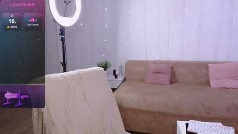 Media: Video of a modern, minimalist living room with a beige sofa, white curtains, and a ring light on a tripod, showcasing a pink and white theme with a soft, cozy ambiance.