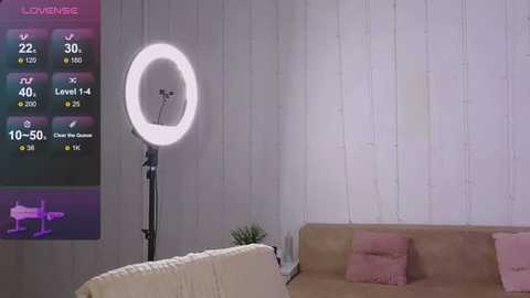 Media: Video of a modern living room with a large, round, bright LED ring light on a stand, white wooden-paneled wall, beige couch, pink pillows, and a digital display showing \"LOVE VIBE\" and fitness stats.