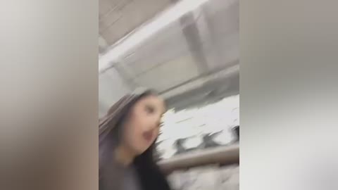 Media: A blurry video of a woman with long dark hair and a grey shirt, standing in a modern kitchen with stainless steel appliances and white cabinets.