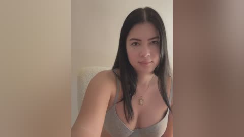 Media: A video of a young woman with long black hair, fair skin, and a slender build, wearing a gray tank top, seated indoors.