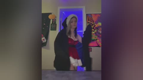 Media: Video of a young woman in a revealing, red Santa outfit with a white fur hood, standing in a dimly lit room adorned with vibrant, abstract art.