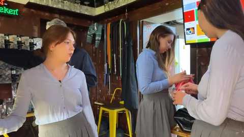 Media: Video of three young women in a cozy, dimly-lit bar, wearing casual clothes; one holds a red cup, another a beer, and the third is looking at a menu.