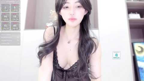 Media: Video of a young, fair-skinned woman with long, wavy black hair, wearing a black lace camisole, showcasing a slender figure and small breasts. Background includes a digital clock and a bookshelf.